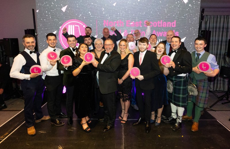 This year's Food and Drink Awards winners wearing evening dress, suits and tartan holding up their awards which are round and pink