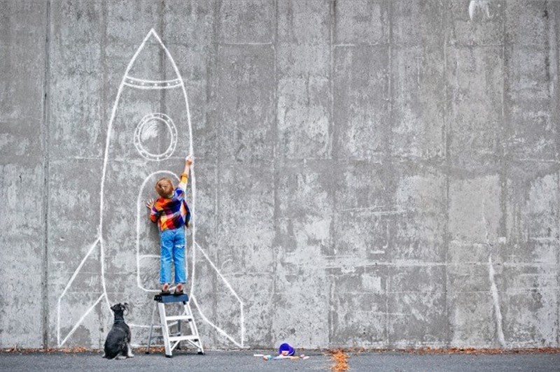 Little boy drawing a space ship on the wall and his dog watching
