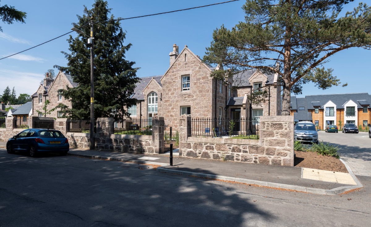 Street view of large stone building with trees and mental fencing