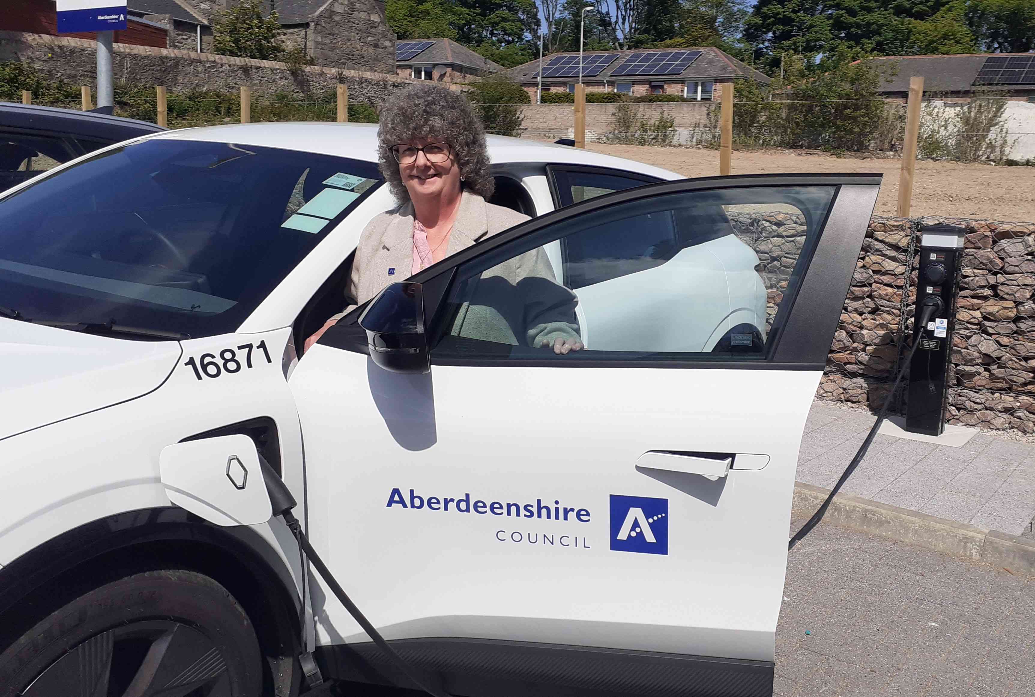 Leader of Aberdeenshire Council Councillor Gillian Owen standing at a white electric vehicle which is plugged into a charging unit