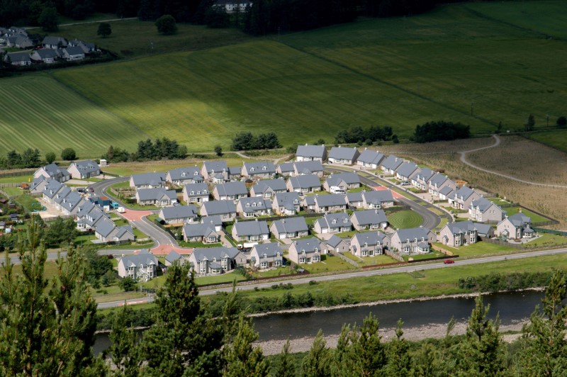 An aerial photograph of a new housing development surrounded by green fields, trees and bordered by a river