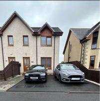 Front of the property at 21 Wellington Drive, tarmac driveway with two cars parked and low wood fence on both sides