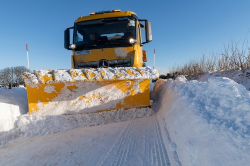 A large yellow gritting lorry plowing through snow